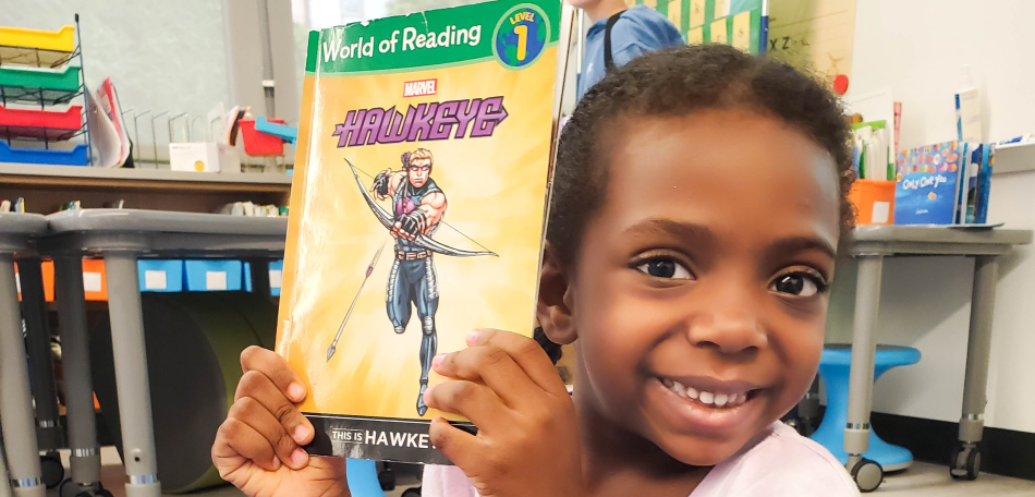 closeup of a young smiling student with braids holding up a book with the title Hawkeye
